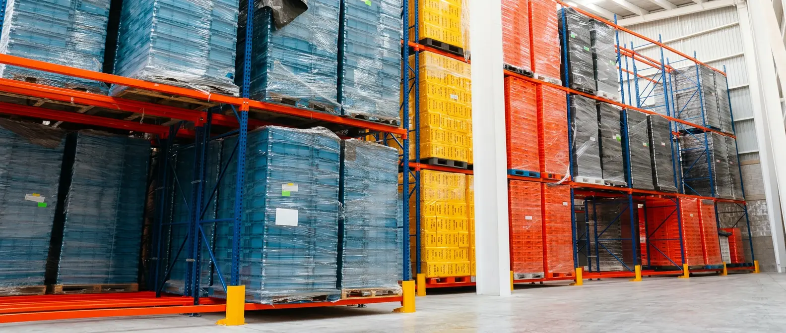 Racks de almacén con cajas de plástico azules, amarillas y rojas estibadas en tarimas